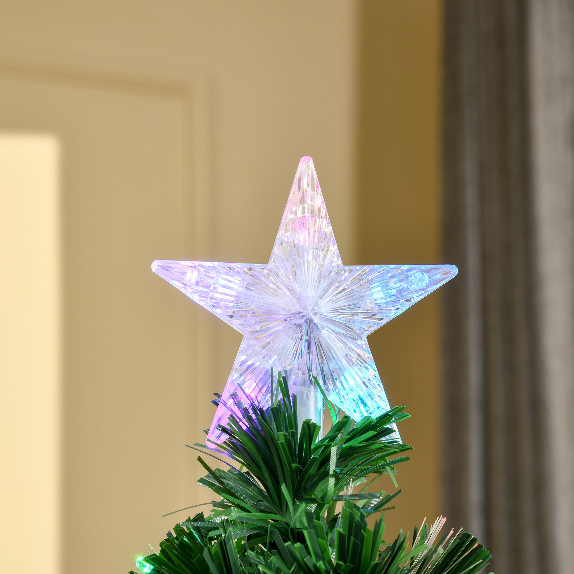 Primer plano de una estrella de árbol de Navidad iluminada con una rama verde. La estrella tiene múltiples colores. Interior.