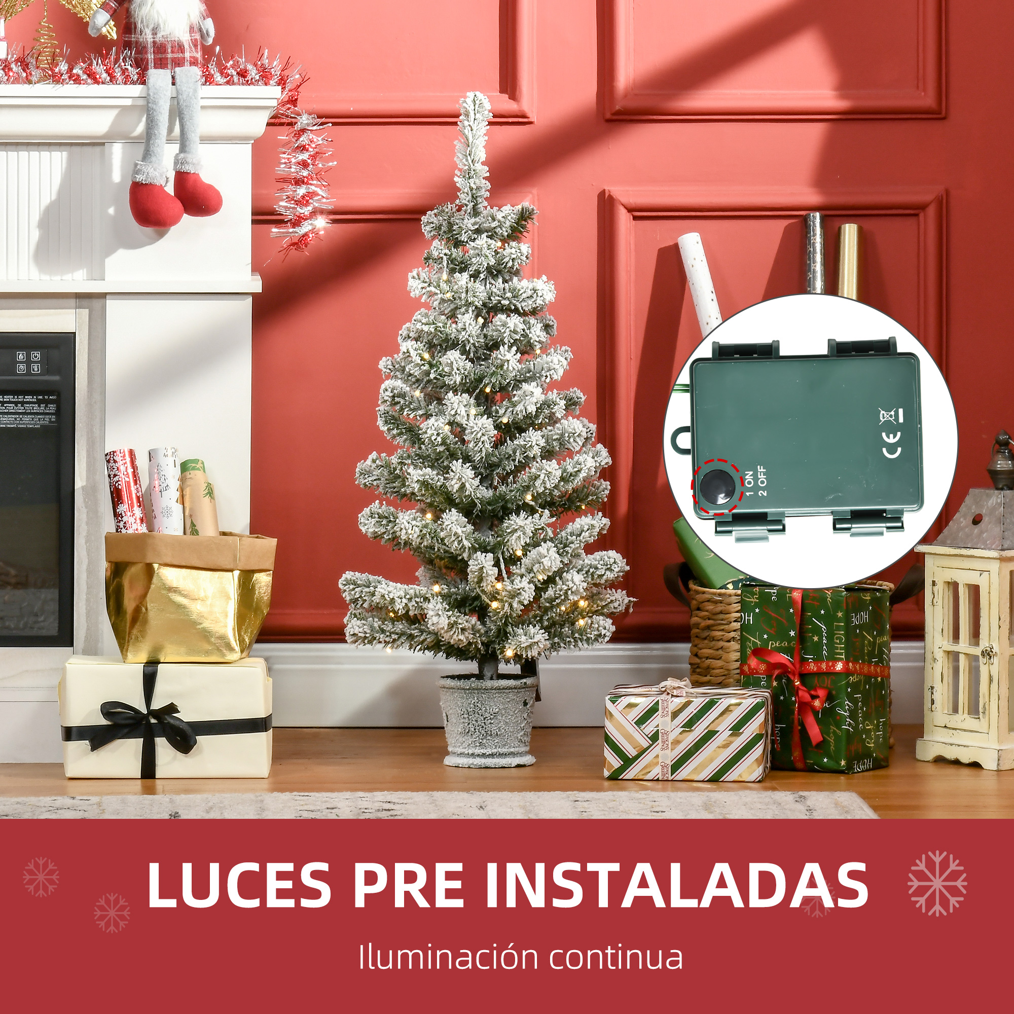 Un árbol de Navidad con luces, regalos y una caja de control, colocado frente a una pared roja.