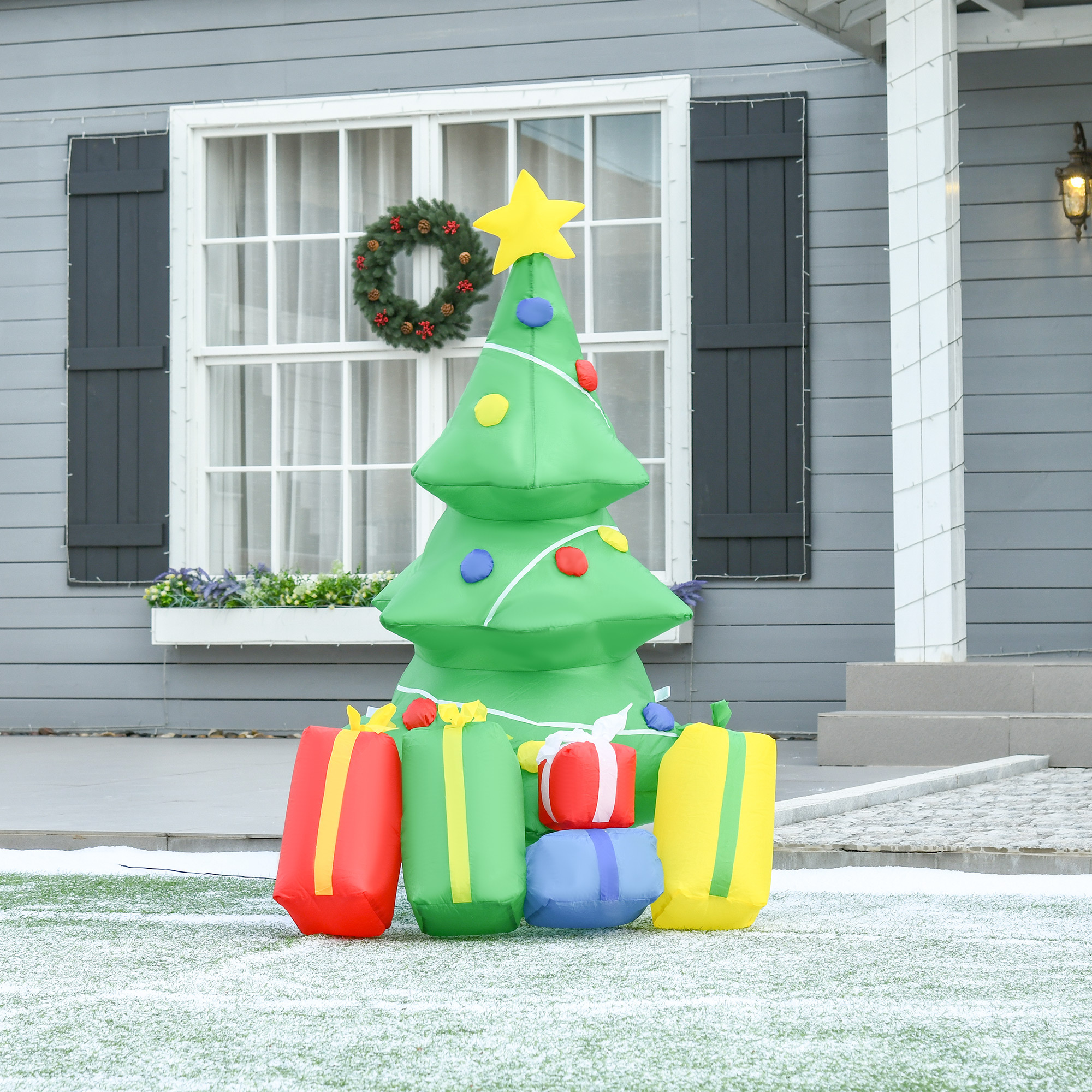 Árbol de Navidad verde inflable con regalos en el césped frente a una casa.