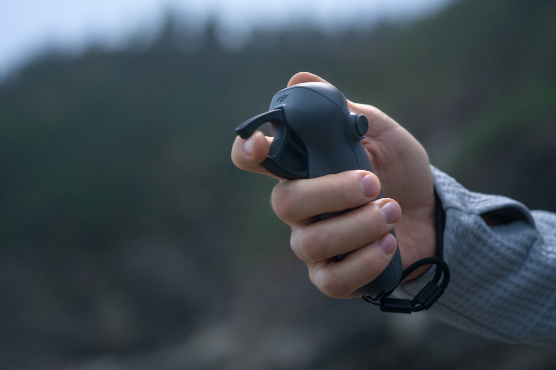 Ręka trzyma czarny kontroler, prawdopodobnie pilota do drona, na rozmytym tle.