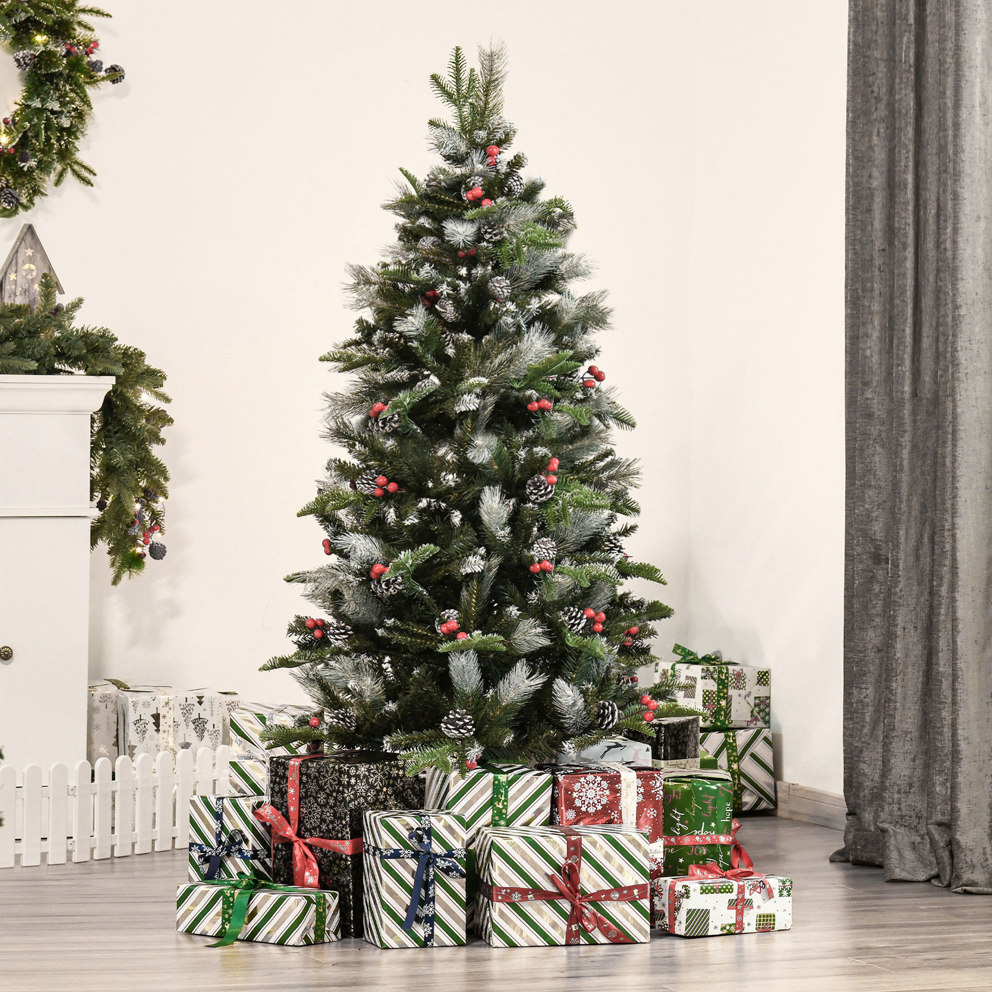 Árbol de Navidad decorado con nieve y bayas rojas, rodeado de regalos envueltos en una habitación.