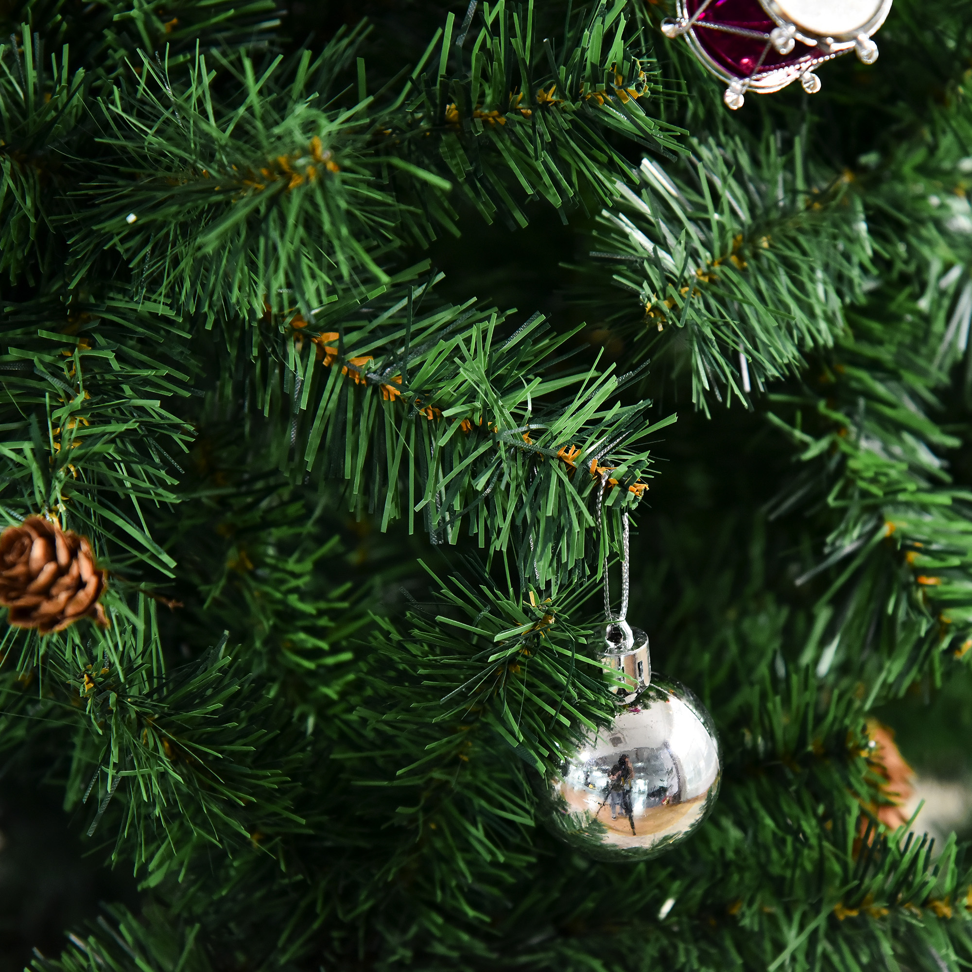Primer plano de un árbol de Navidad verde con adorno de bola plateada y decoración de piñas.