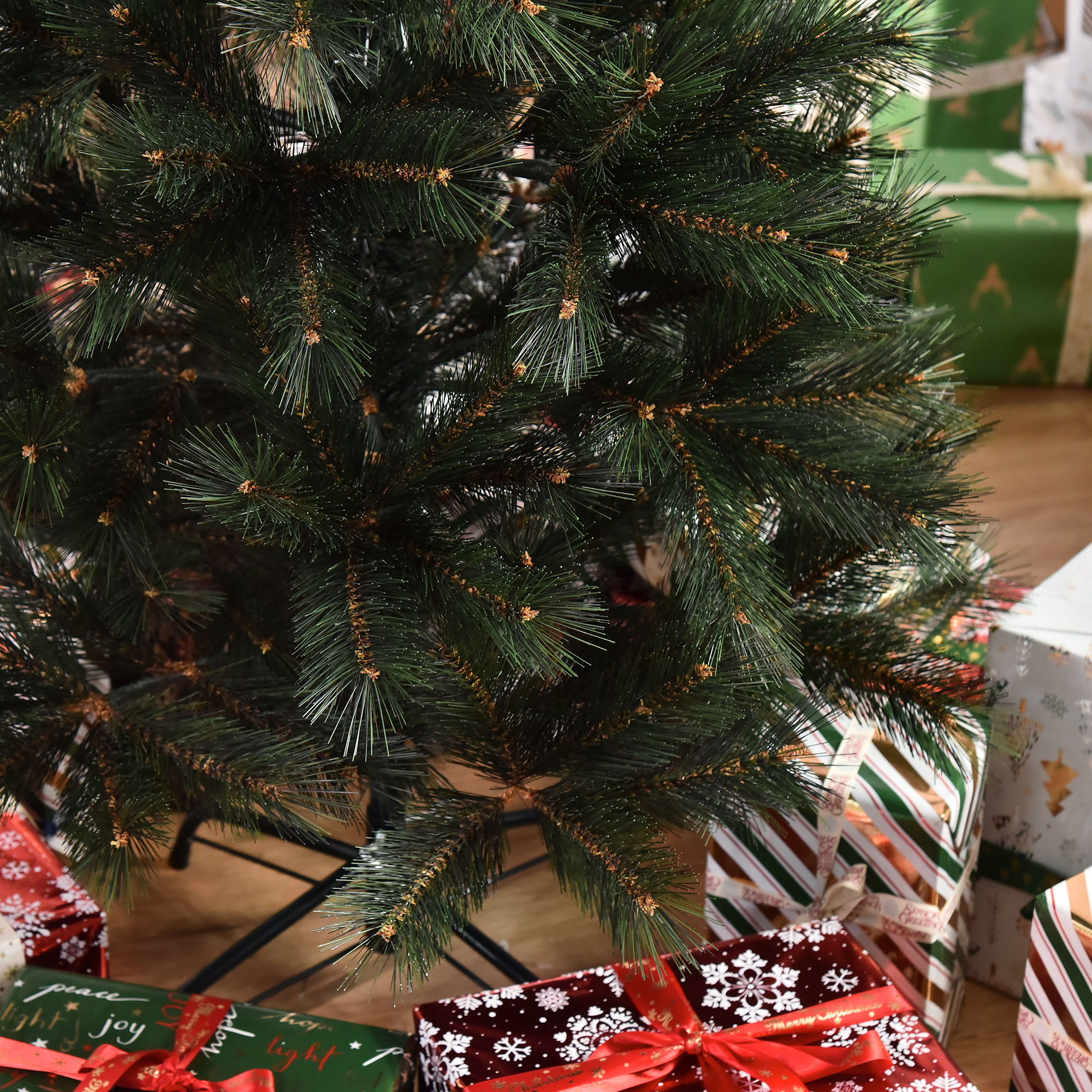 Primer plano de un árbol de Navidad con agujas verdes y regalos en el fondo borroso.