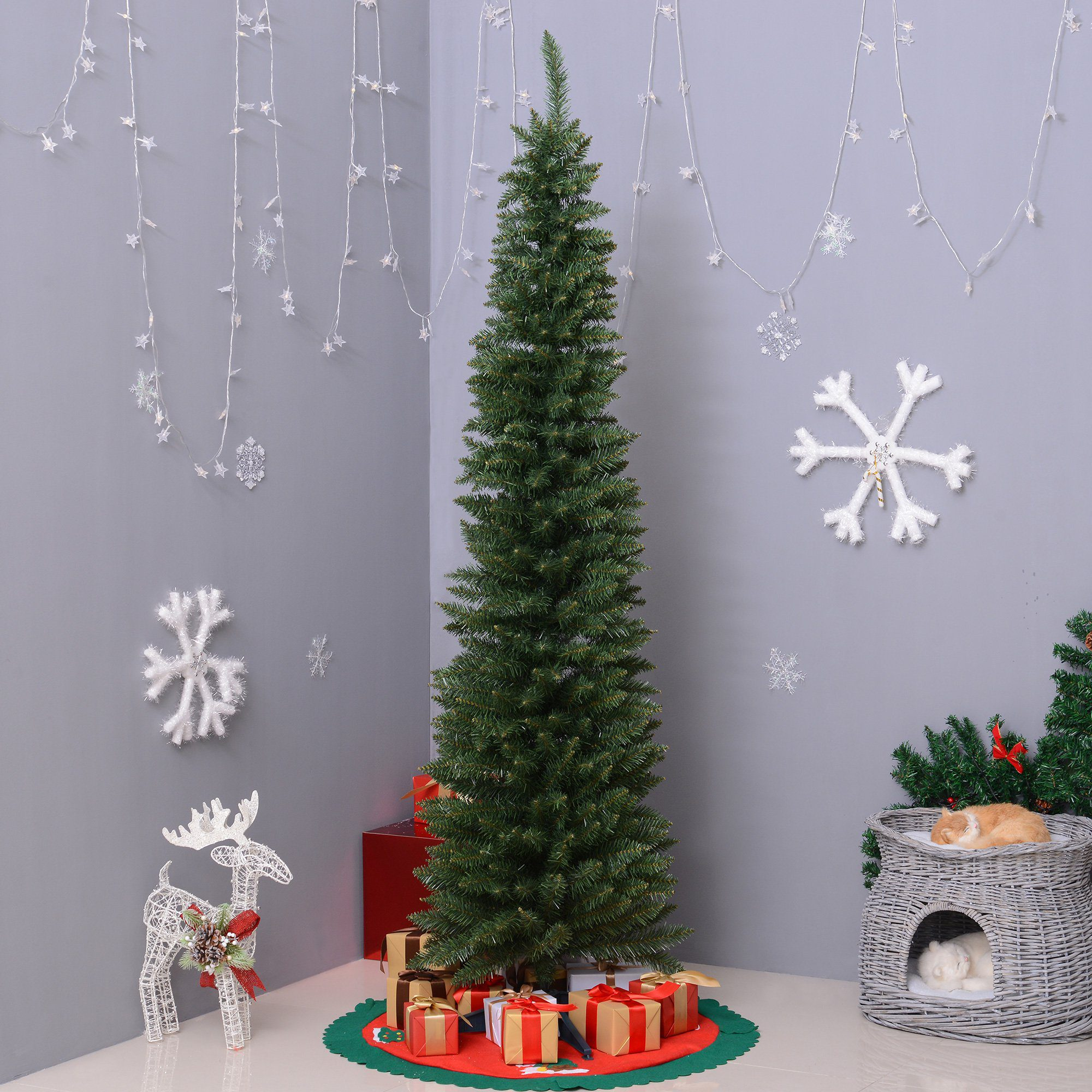Un árbol de Navidad delgado con regalos, copos de nieve y una cama para gatos en una habitación.
