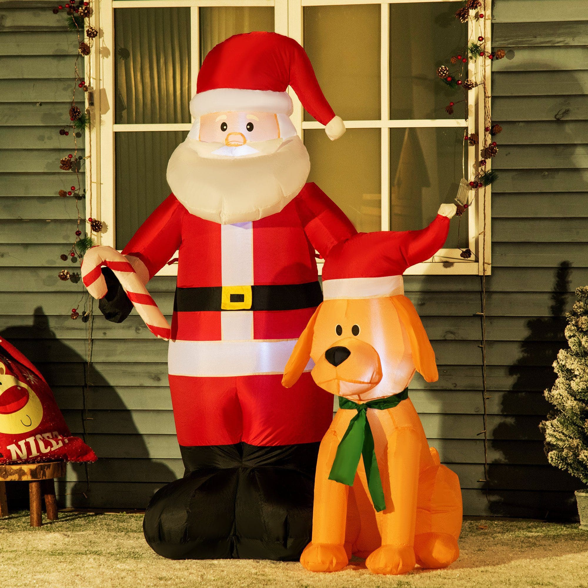 Decoraciones inflables de Papá Noel y perro. Escena sobre hierba verde con una casa al fondo.