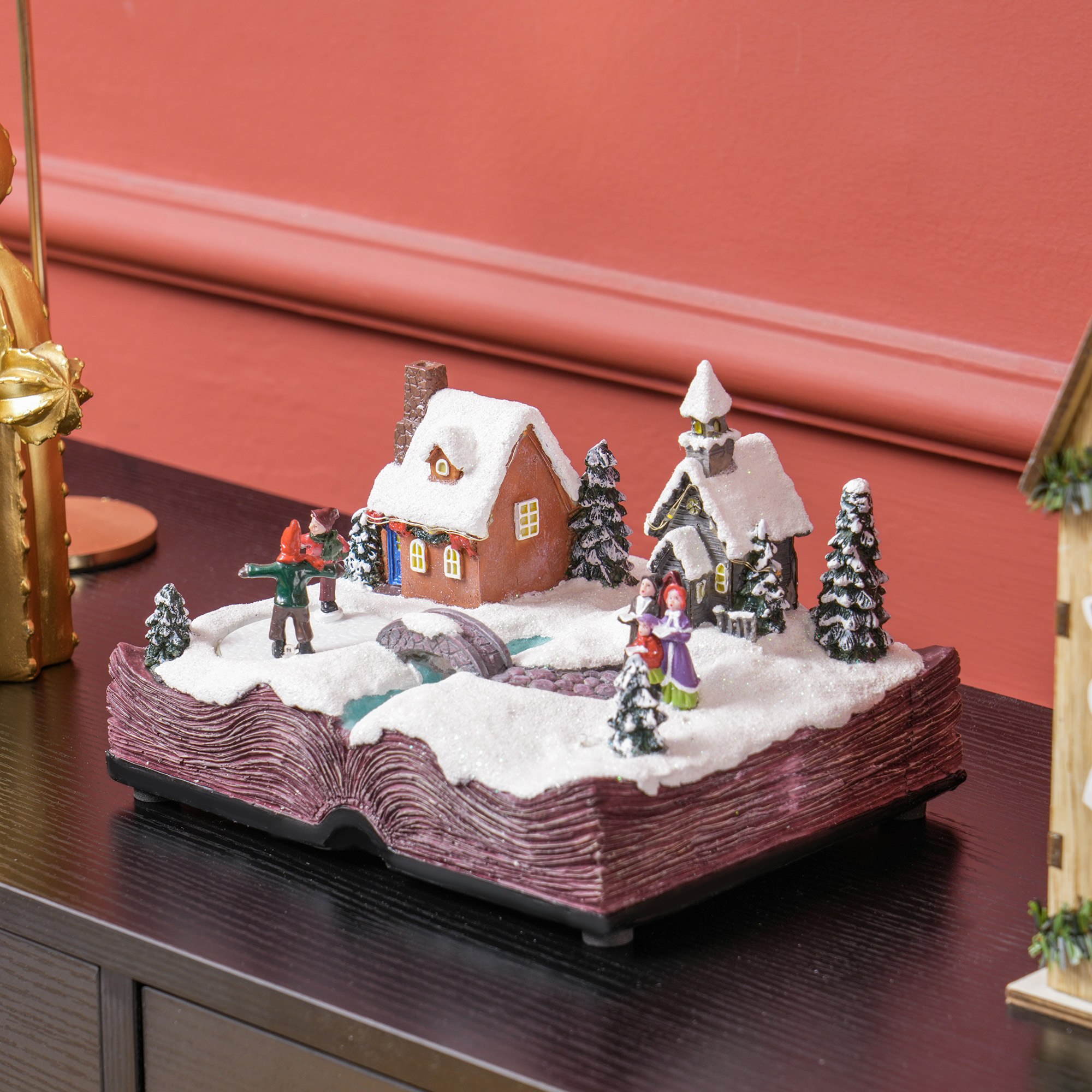 Diorama de escena navideña en base de libro, con casas, figuras y nieve.