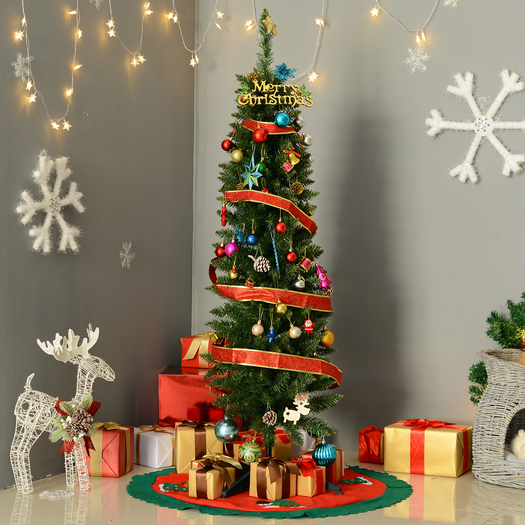 Un árbol de Navidad alto y decorado con regalos y adornos, contra una pared gris.