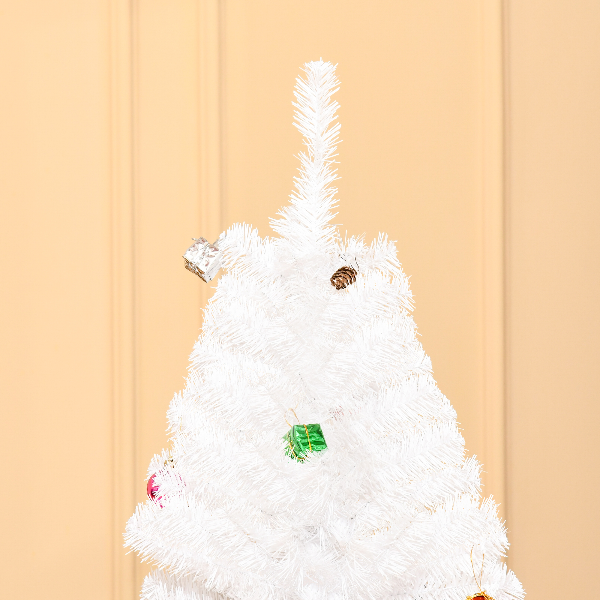 Primer plano de la parte superior de un árbol de Navidad blanco con adornos. Unos cuantos adornos lo decoran.