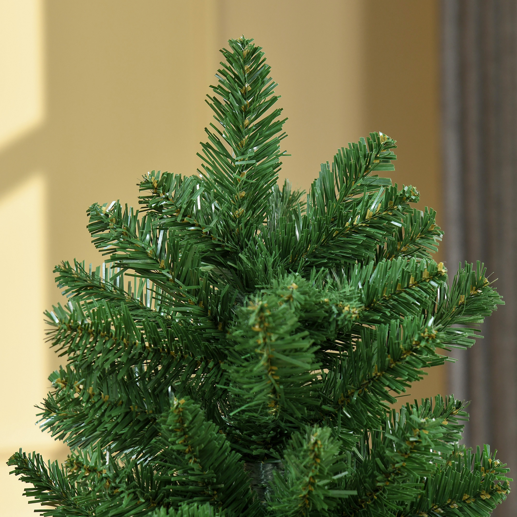 Primer plano de ramas de árbol de Navidad, agujas verdes. El fondo es una pared suave, borrosa y de tonos amarillos.