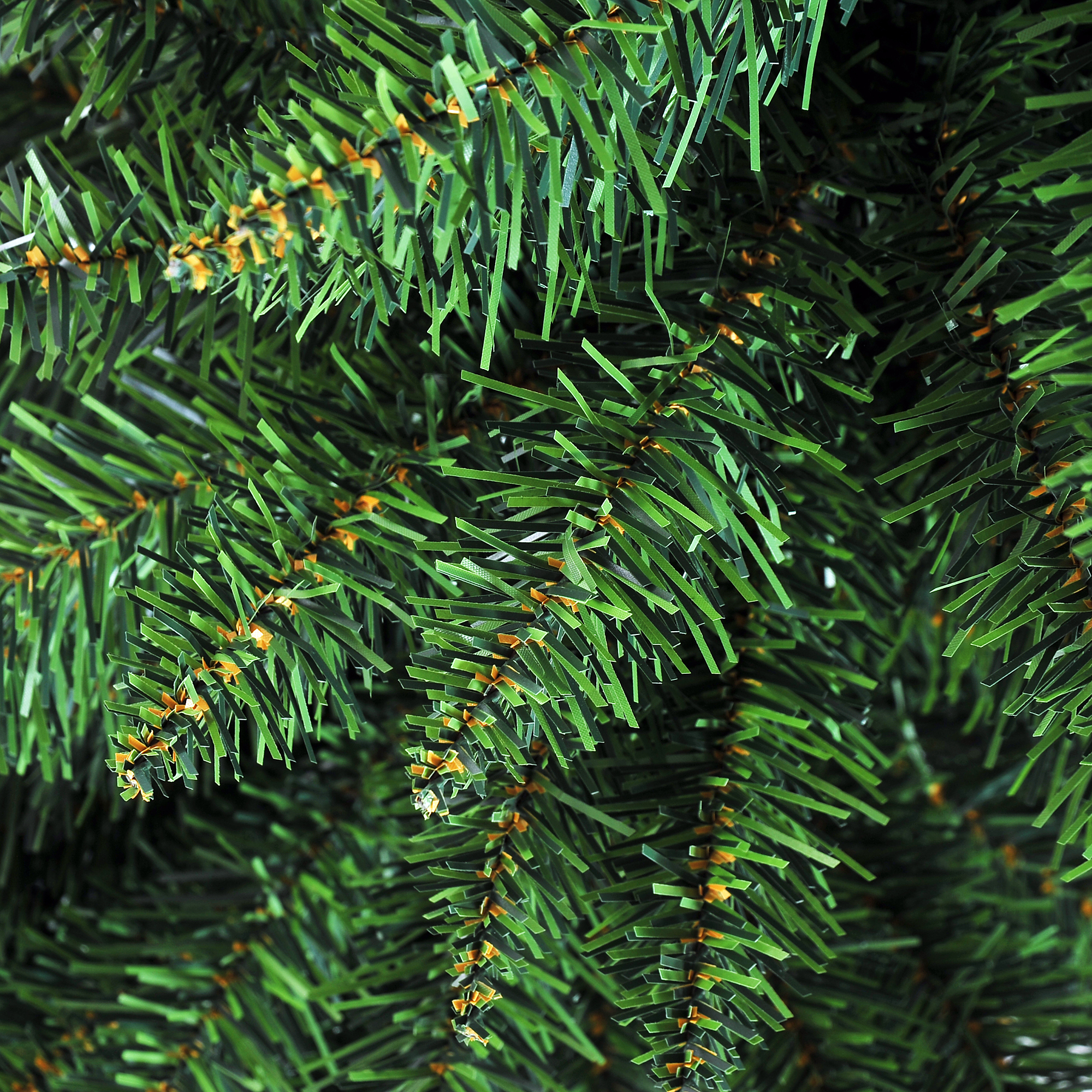 Primer plano de ramas verdes de árbol de Navidad artificial con pequeños acentos naranjas.