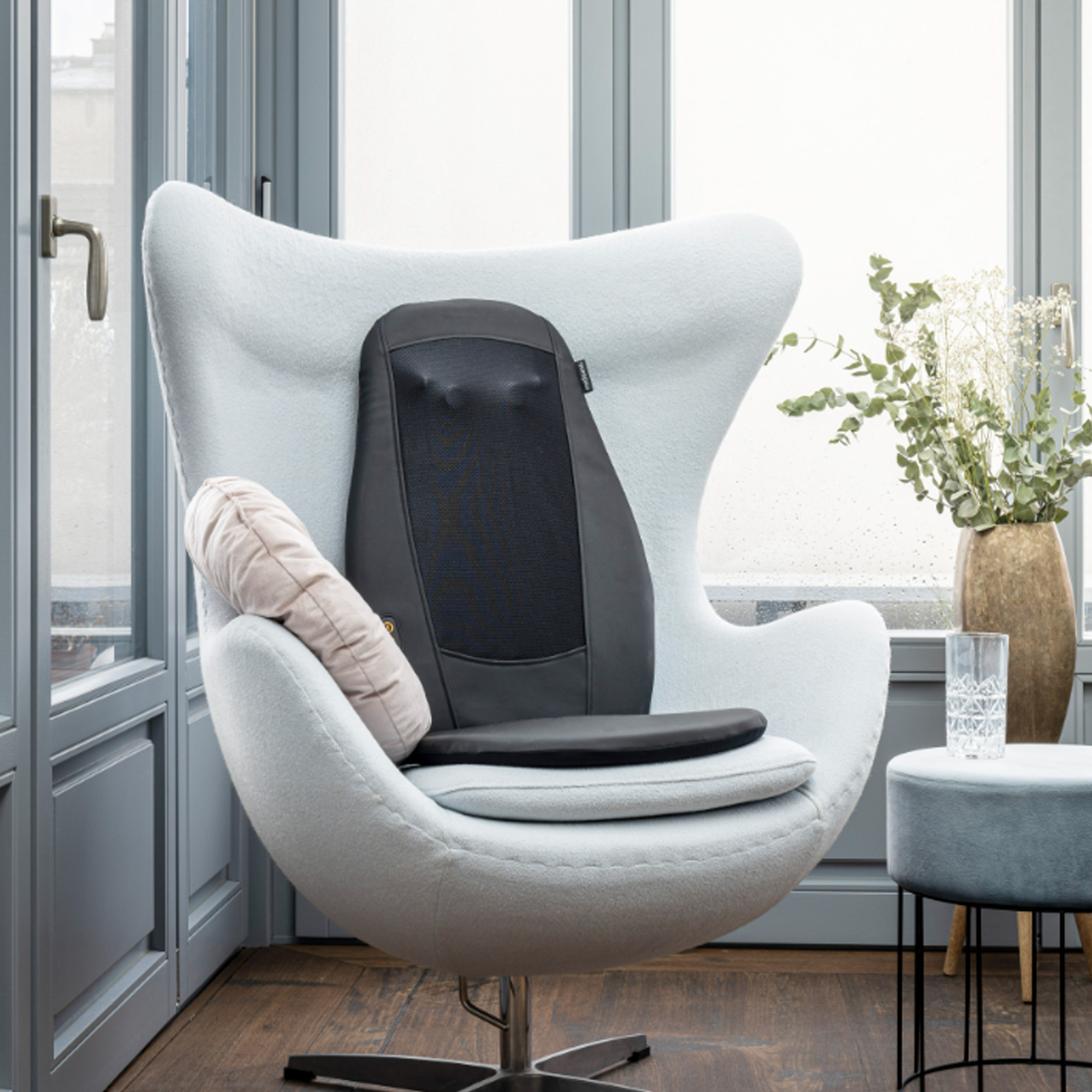 Silla huevo blanca moderna con cojín de masaje negro, almohada y mesita auxiliar.