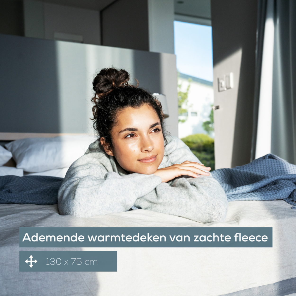 Frau mit Dutt schaut aus dem Fenster, sitzt auf einem Bett. Text auf Niederländisch.