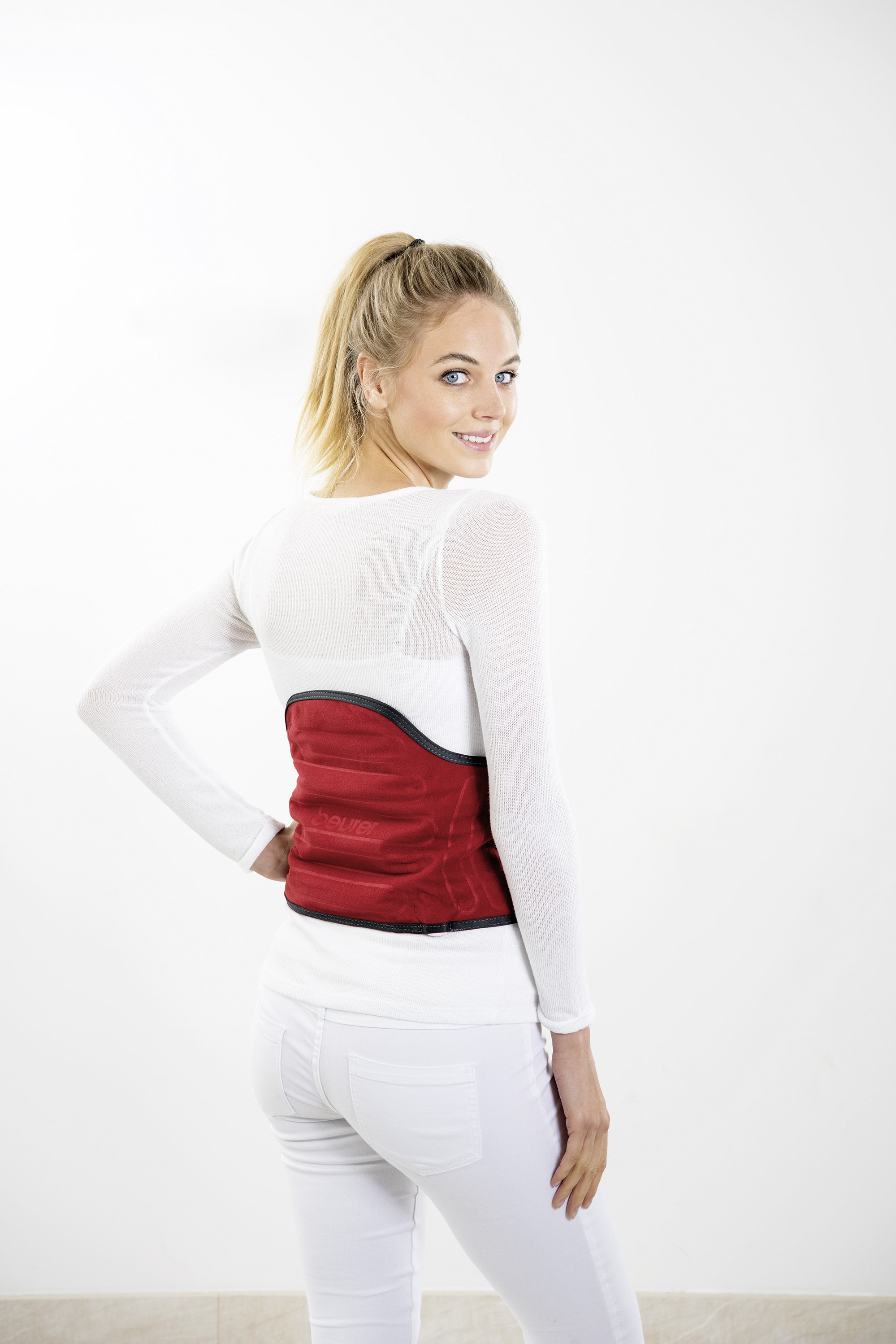Frau in weißem Oberteil und Hose, mit rotem Rückenstützgürtel, lächelnd, heller Hintergrund.