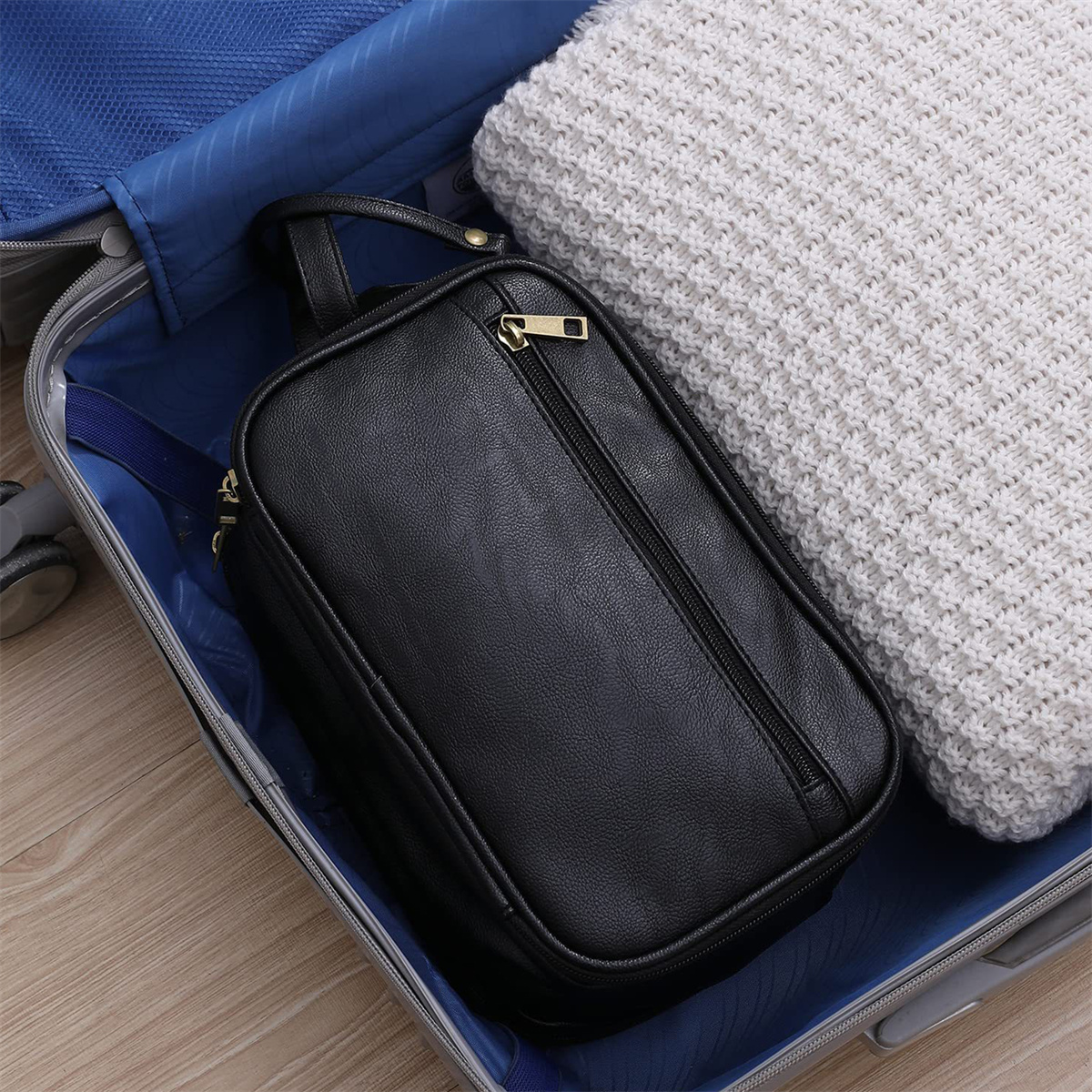 Eine schwarze Kulturtasche mit goldenem Reißverschluss in einem Koffer mit einem weißen Pullover.