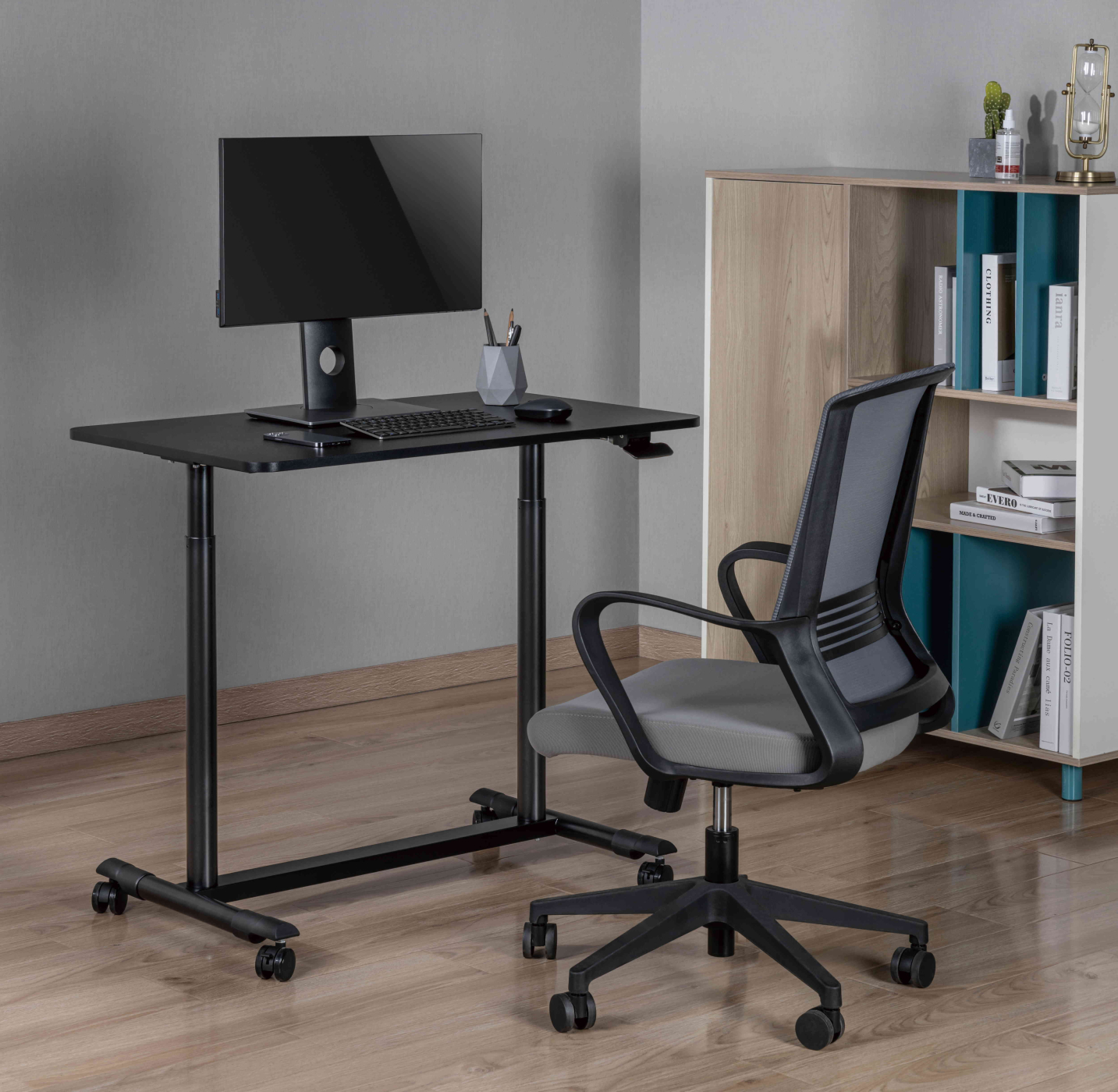 Een zwart bureau met een monitor, toetsenbord en stoel. Een kast op de achtergrond.