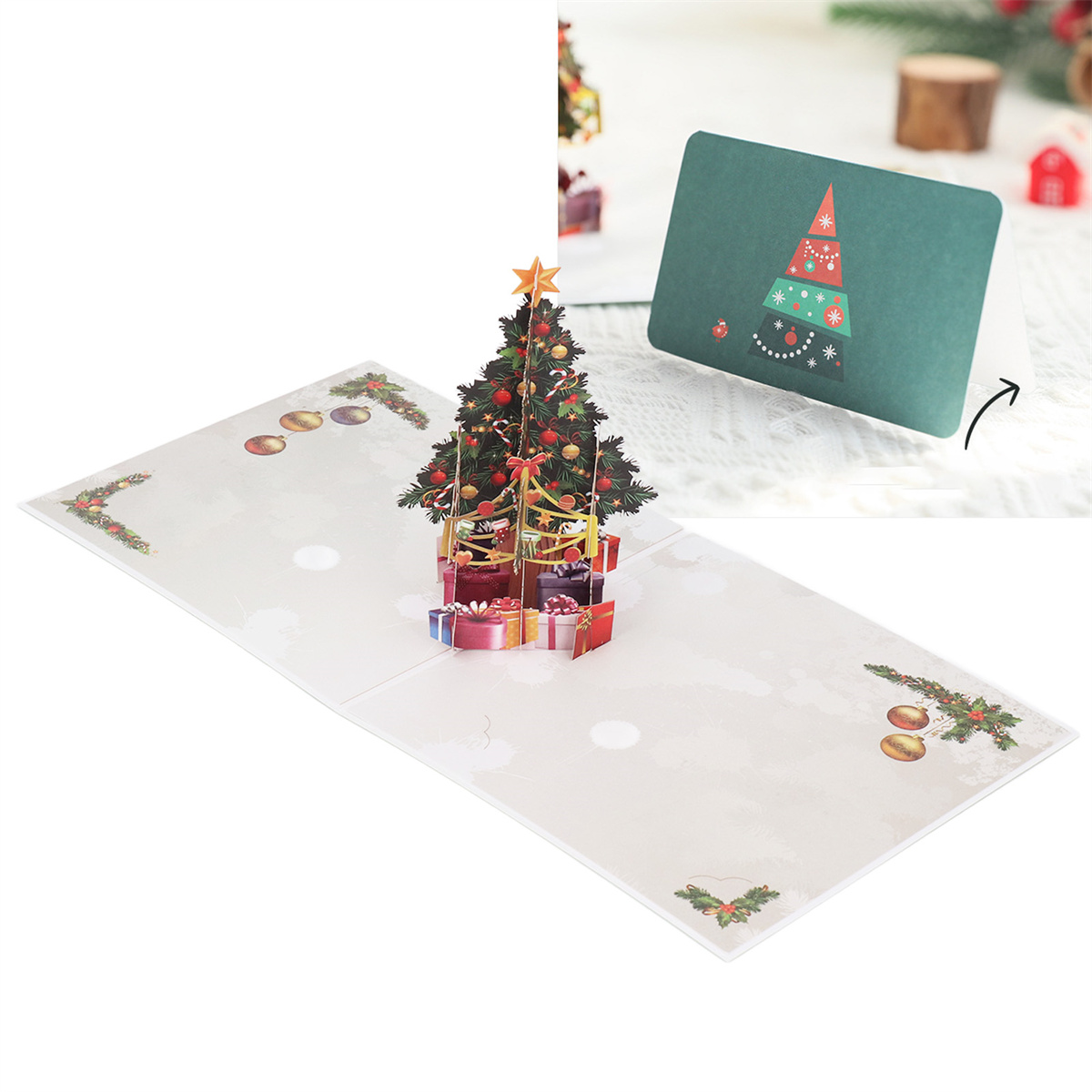 Eine Pop-up-Weihnachtskarte, geöffnet, um einen Weihnachtsbaum und Geschenke zu zeigen. Eine Karte ist im Hintergrund.