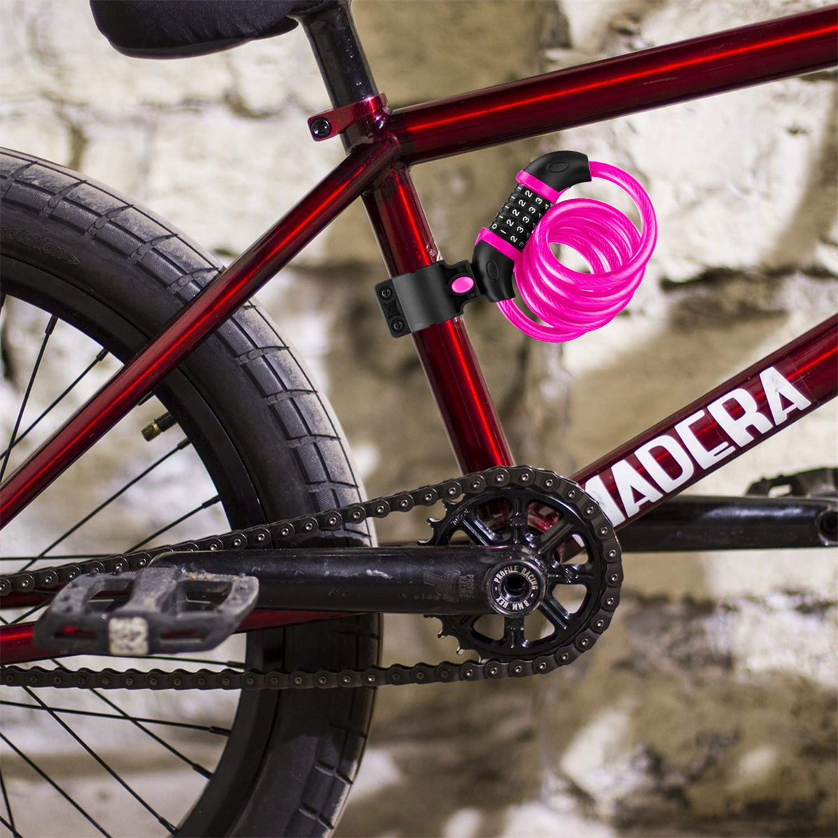 Rotes Fahrrad mit einem pinkfarbenen Zahlenschloss. Schloss ist um den Rahmen gewickelt. Fahrrad steht an einer Backsteinmauer.