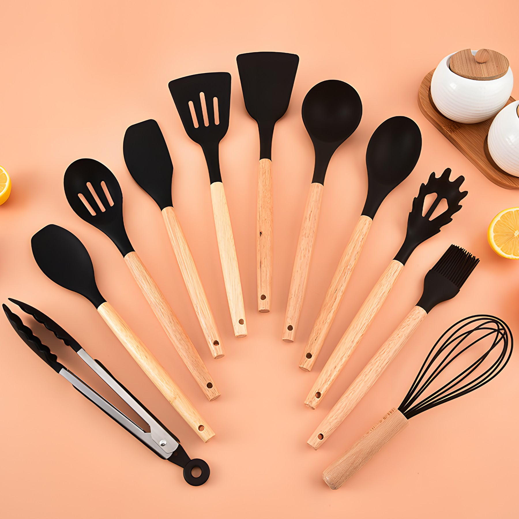 Küchenutensilien auf rosa Oberfläche angeordnet. Enthält Löffel, Spatel, Zangen, Schneebesen und Pinsel, mit Holzgriffen.