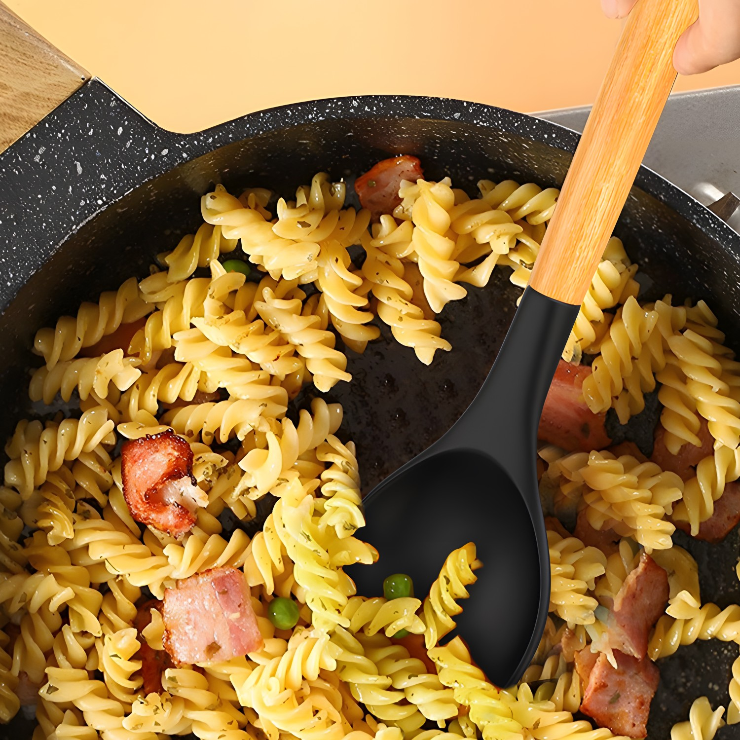 Pasta mit Speck und Erbsen in einer Pfanne. Ein schwarzer und hölzerner Löffel darin.