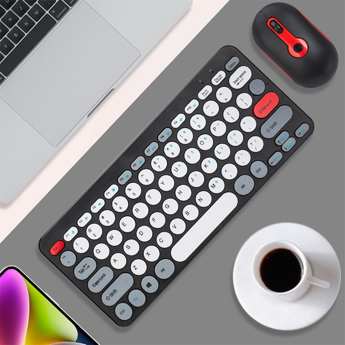Kabellose Tastatur, Maus und eine Tasse Kaffee auf einem Schreibtisch. Ein Smartphone und ein Laptop sind ebenfalls zu sehen.