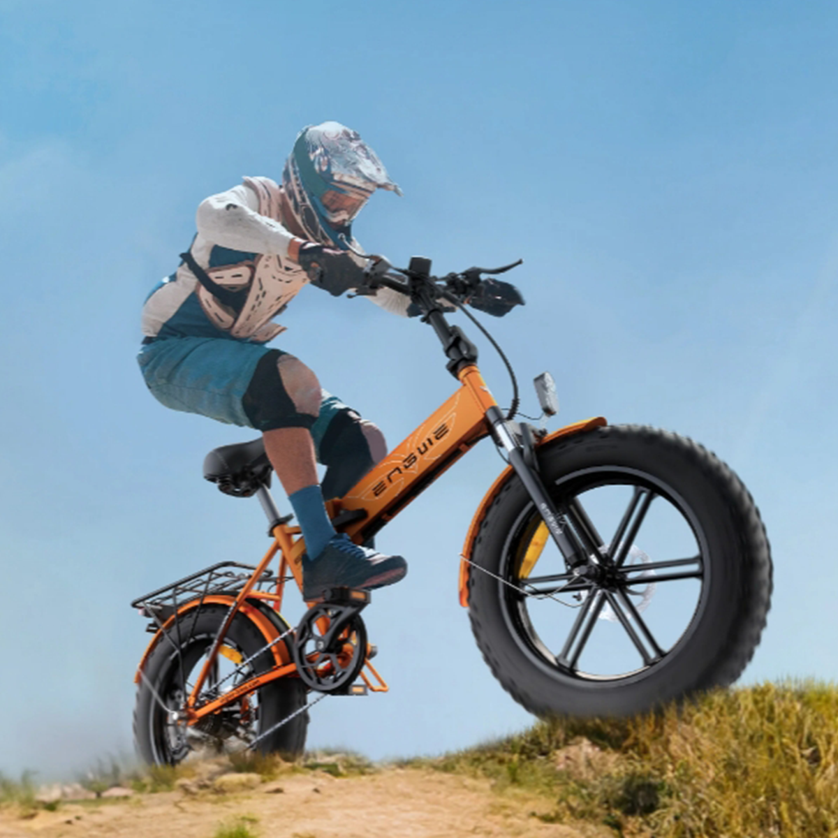 Un uomo che guida una mountain bike elettrica arancione e nera su uno sterrato contro un cielo blu.
