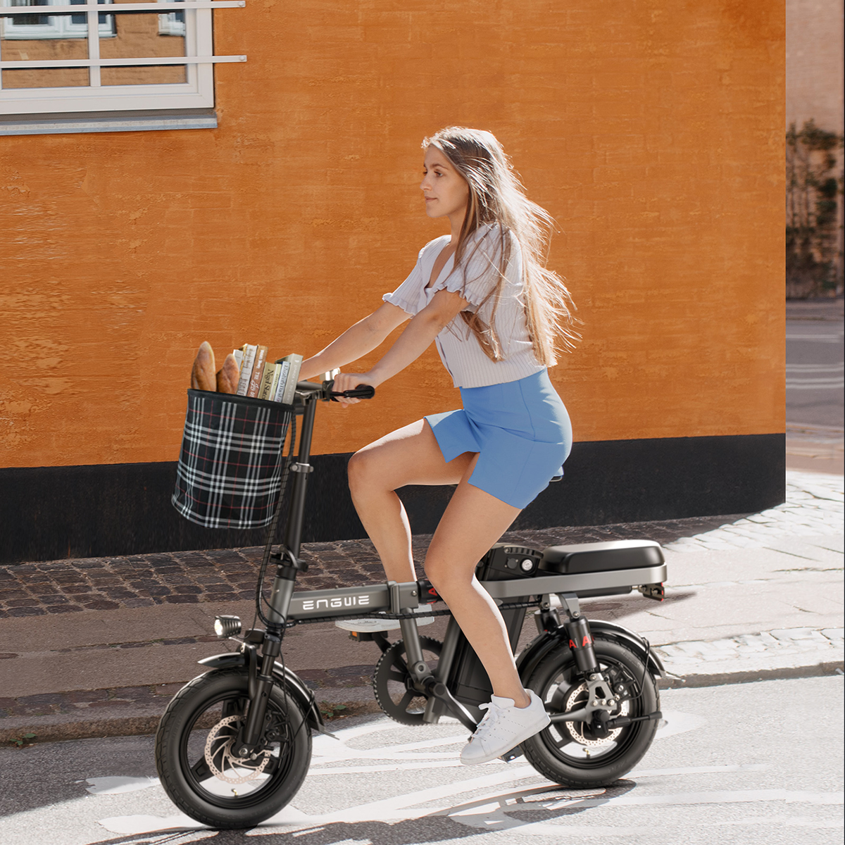 Kobieta jadąca czarnym rowerem elektrycznym z koszem na ulicy.
