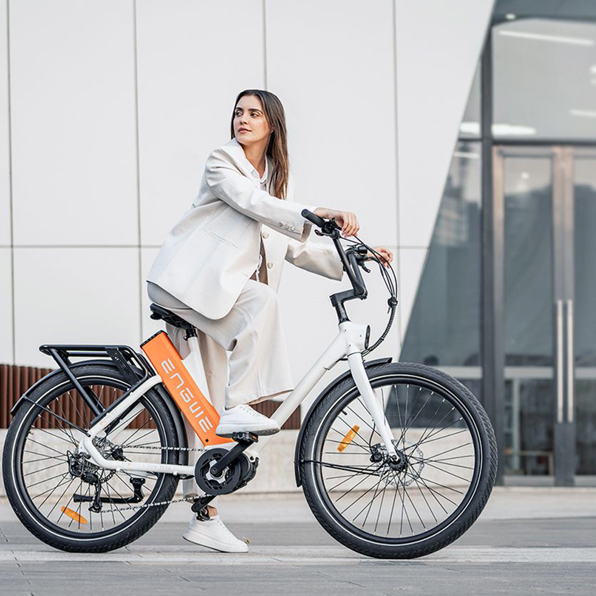 Kobieta jadąca biało-czarnym rowerem elektrycznym na ulicy. Rower ma pomarańczowe logo.