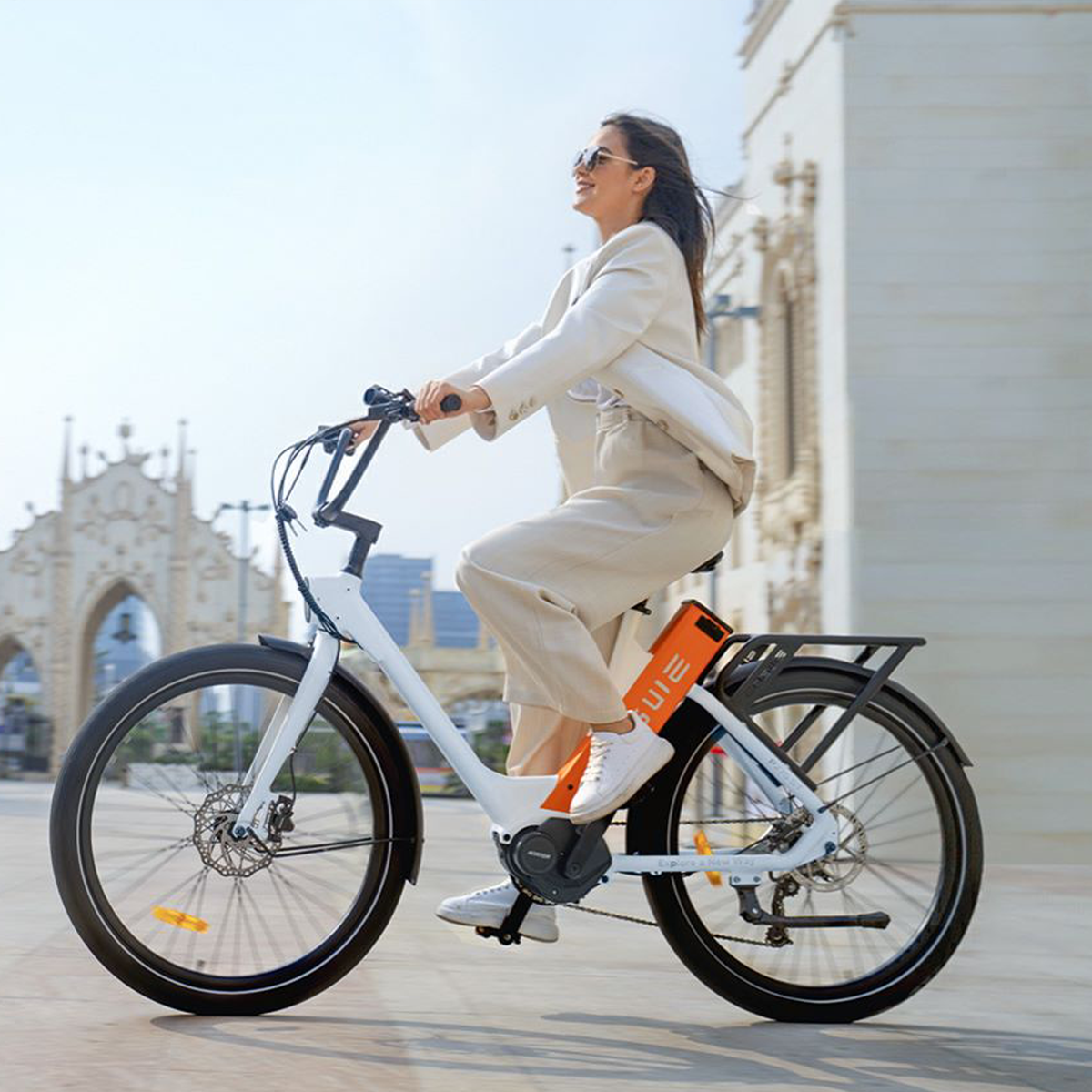 Kobieta jadąca na białym rowerze. Nowoczesny budynek w tle, słoneczny dzień.