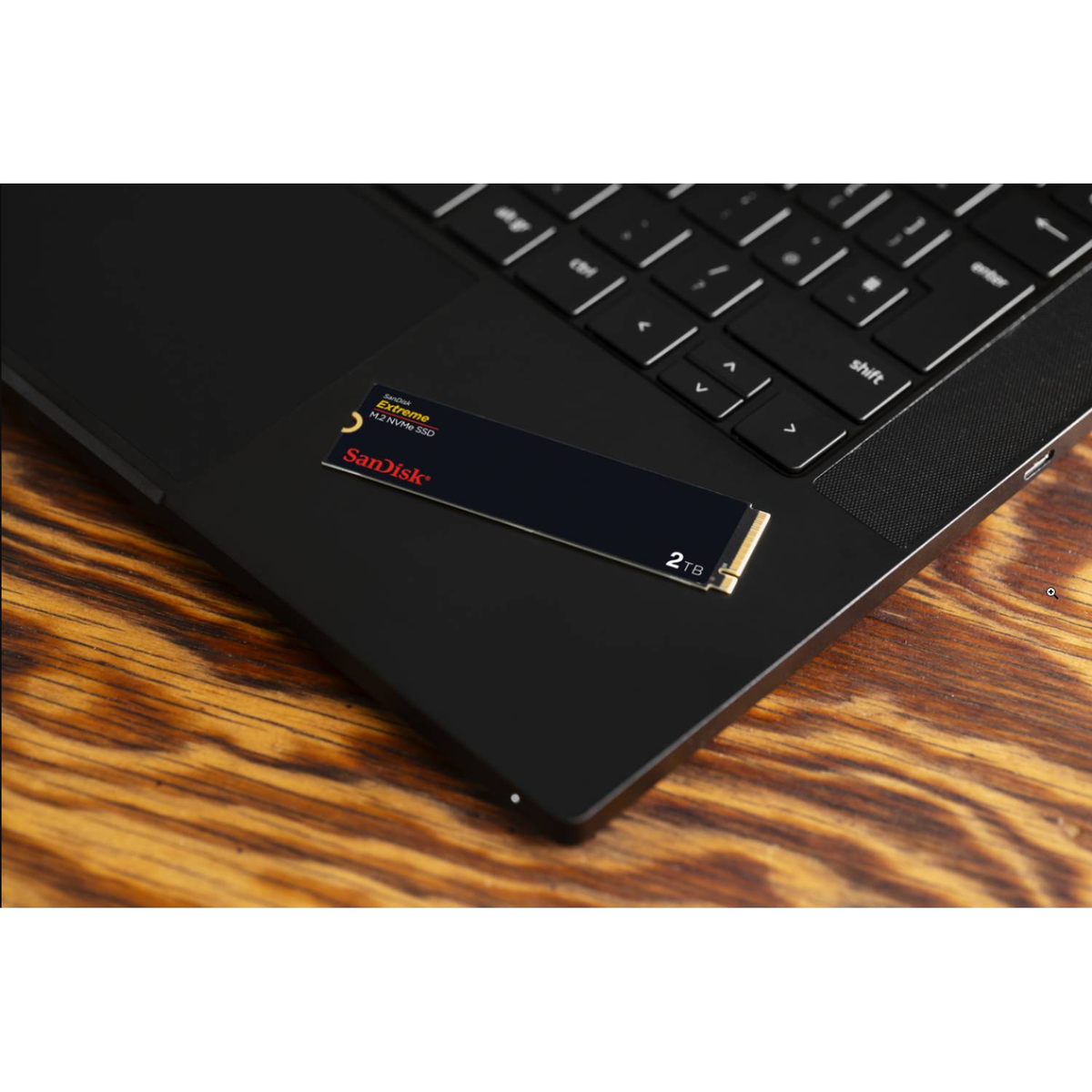 Czarny laptop z dyskiem SSD SanDisk 2TB na wierzchu i czarną powierzchnią.