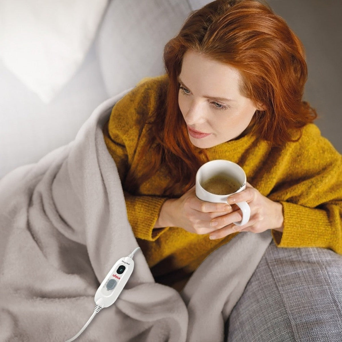 Mujer envuelta en manta, sosteniendo taza. Controlador manta eléctrica.