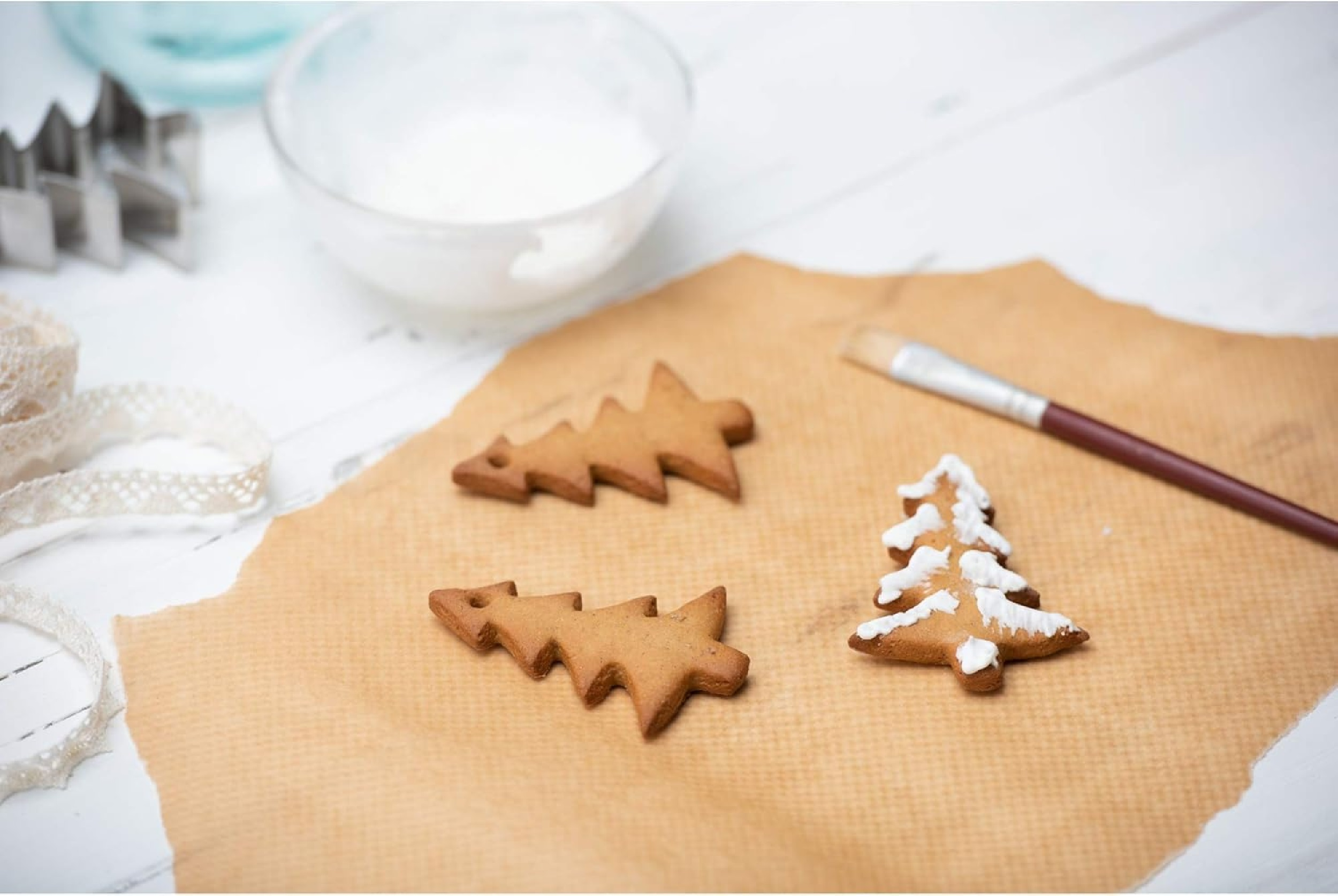 Lebkuchen-Weihnachtsbäume mit weißem Zuckerguss verziert, auf braunem Papier, mit Pinsel.