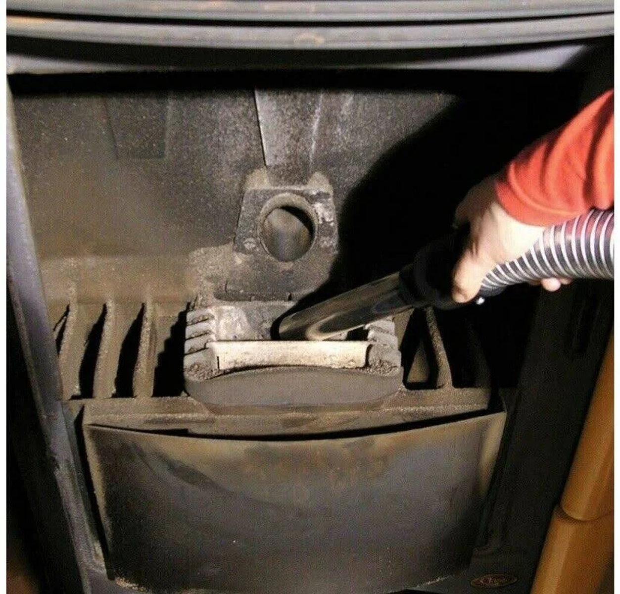 Persona che aspira l'interno di una stufa con un tubo.