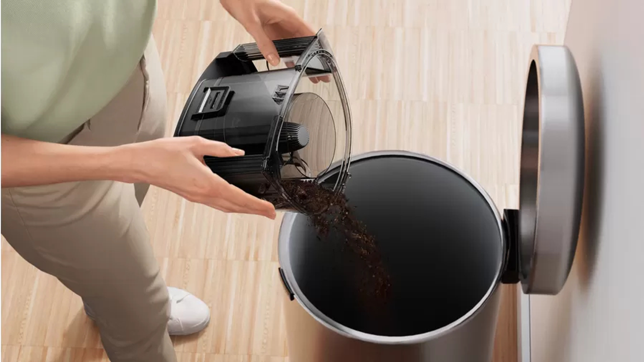 Osoba opróżniająca pojemnik na kurz z odkurzacza do kosza na śmieci, w pomieszczeniu, z bliska.