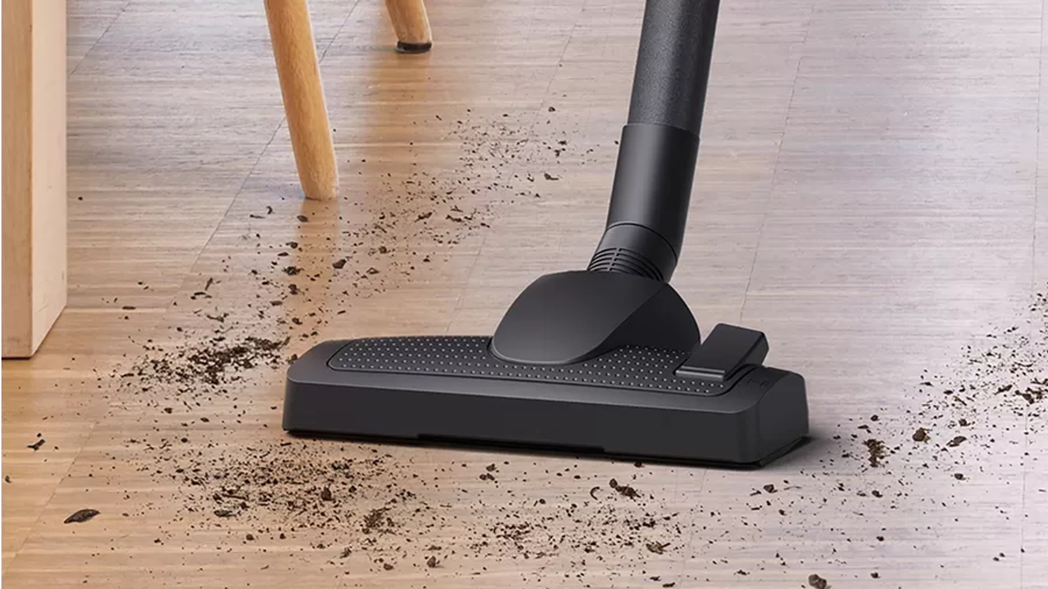 Czarna głowica odkurzacza na drewnianej podłodze z brudem wokół.