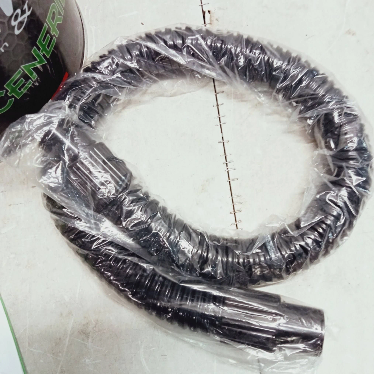 Un tubo per aspirapolvere nero, arrotolato e avvolto in plastica trasparente. Il tubo è ondulato.