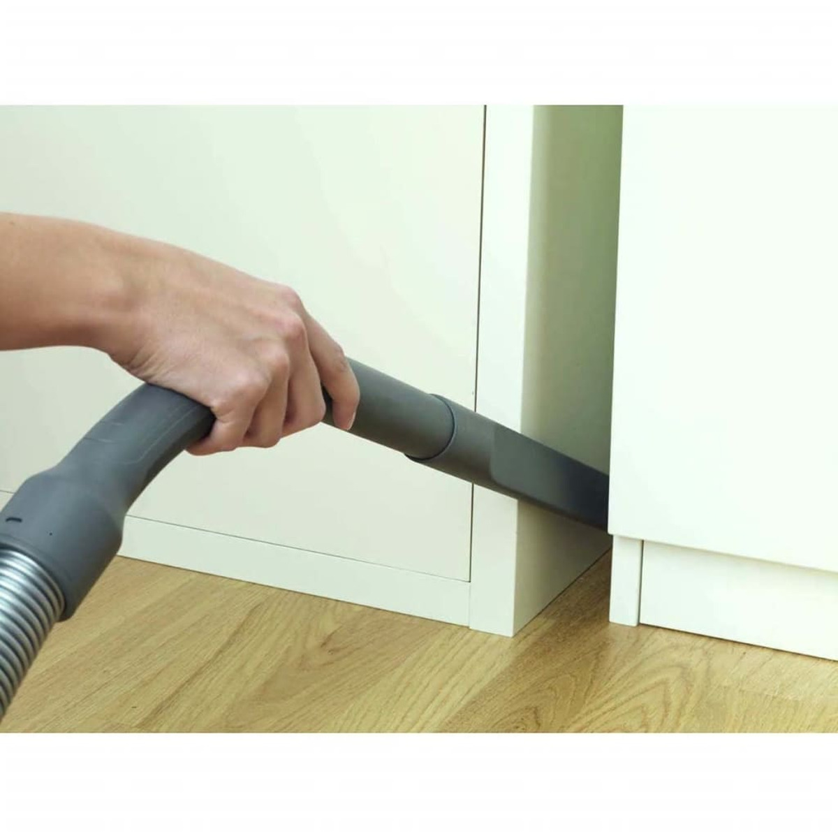 Ręka odkurza róg. Dysza odkurzacza jest szara, a podłoga drewniana.