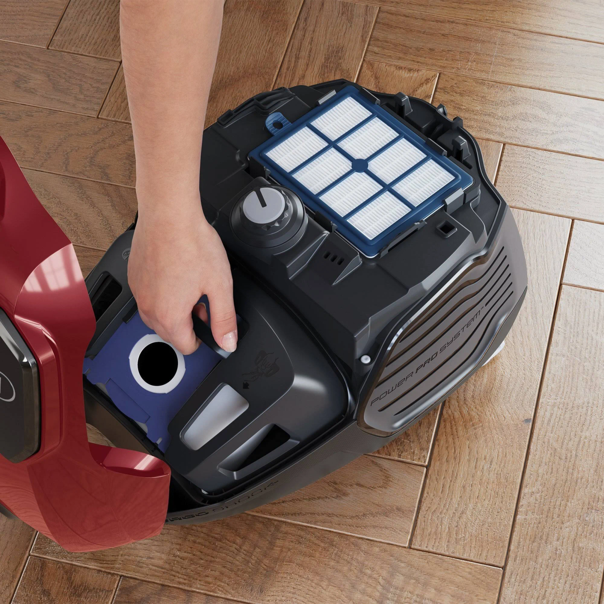 A person's hand removing a filter from a black vacuum cleaner on a wooden floor.