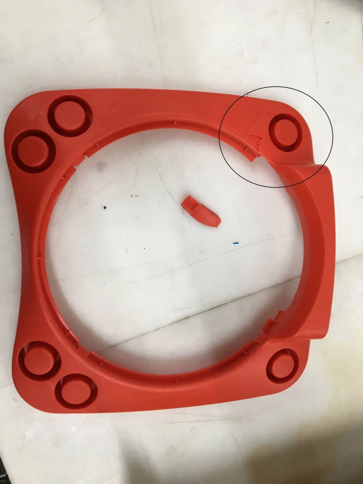 Un anello di plastica rosso rotto con fori e un pezzo staccato, su una superficie bianca.