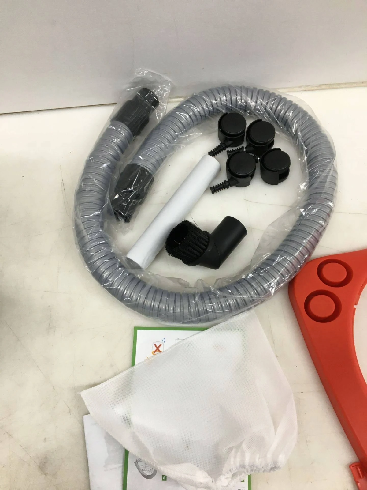 Accessori per aspirapolvere: tubo, spazzole, rotelle e sacchetto filtro.