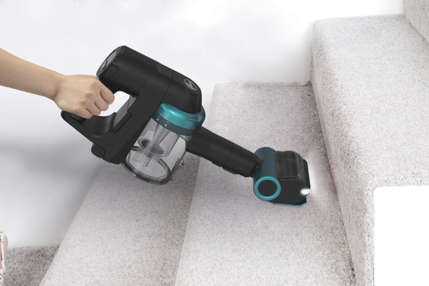 Osoba odkurza schody dywanowe czarno-turkusowym odkurzaczem bezprzewodowym.