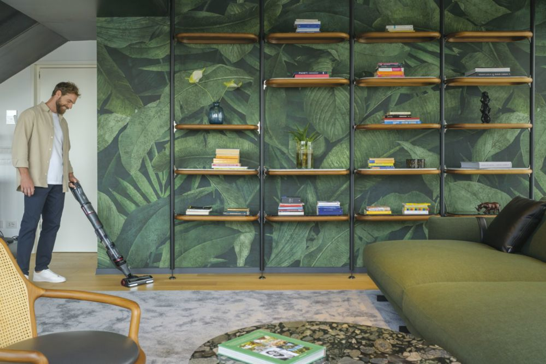 Hombre aspirando una habitación con pared verde estampada y suelo de madera.