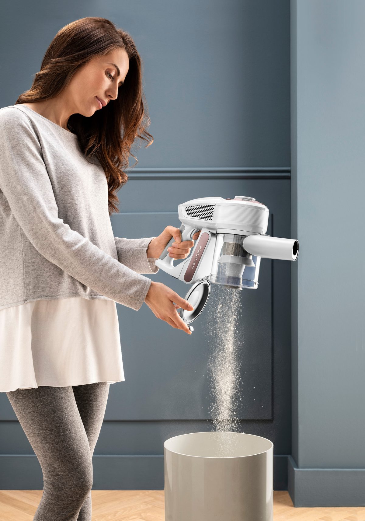 Donna che svuota un aspirapolvere portatile bianco e grigio in un cestino bianco.