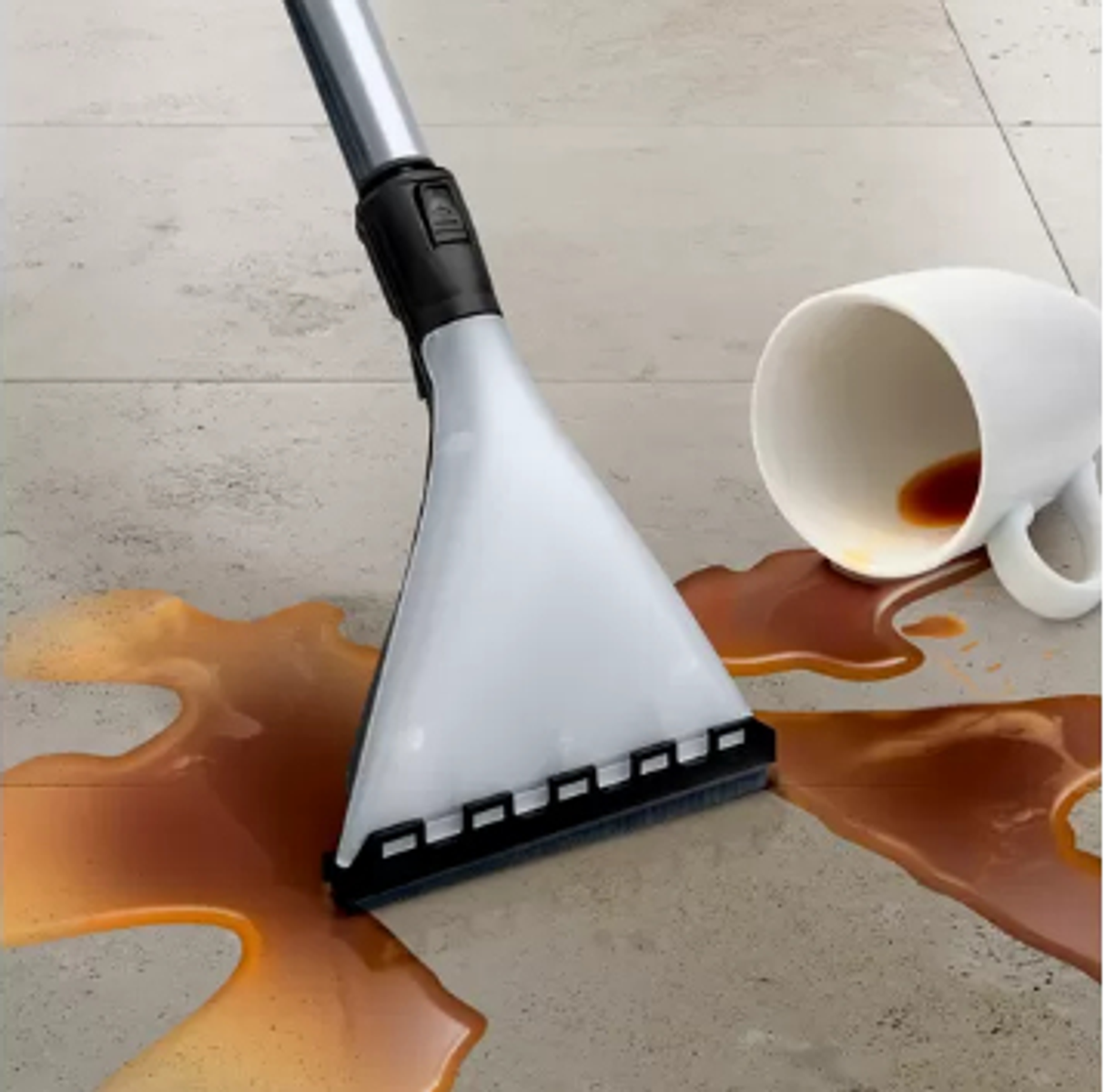 Cabezal de aspiradora limpiando café derramado, taza blanca cerca.