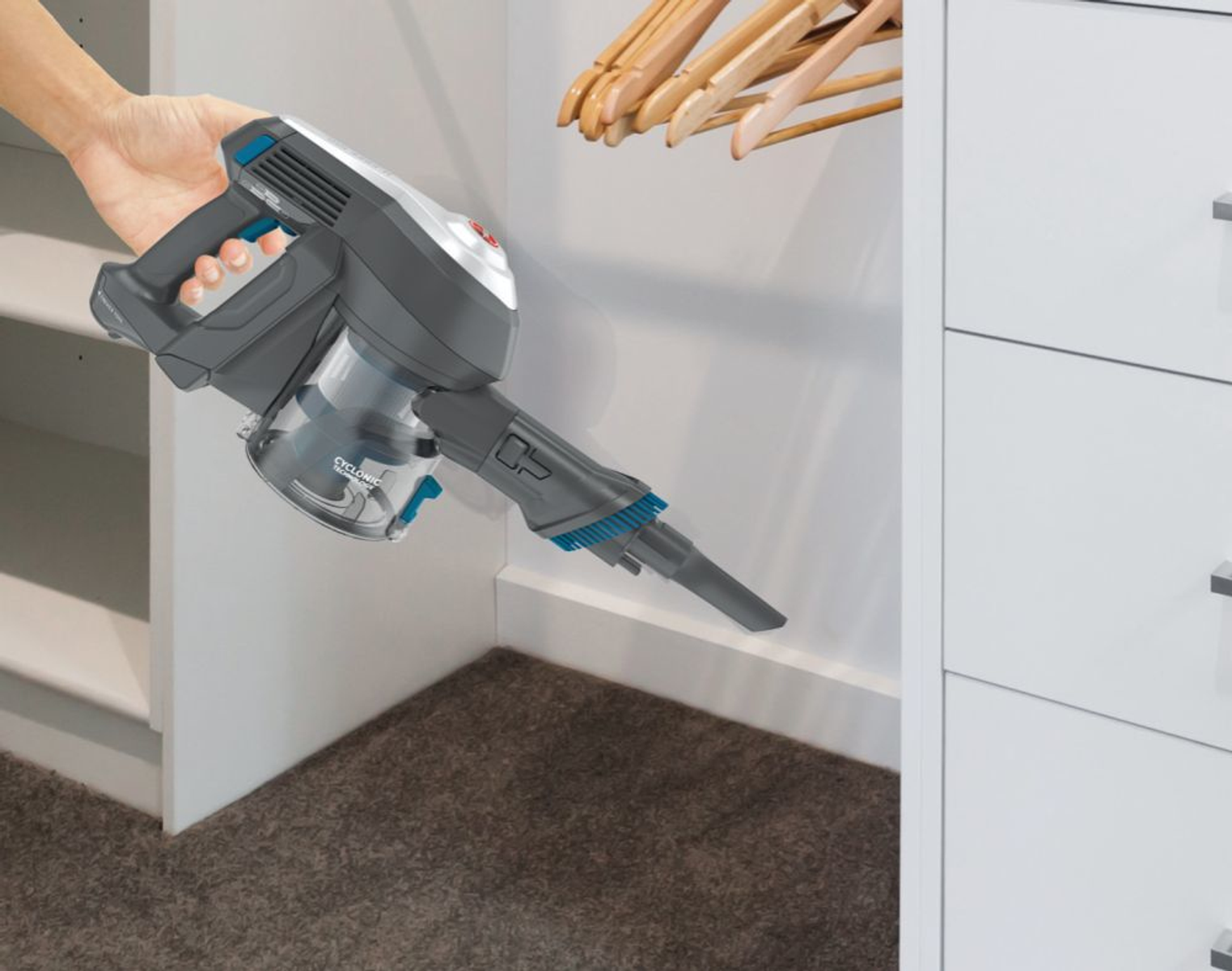 Hand hält einen grau-schwarzen kabellosen Staubsauger und reinigt einen weißen Schrank.
