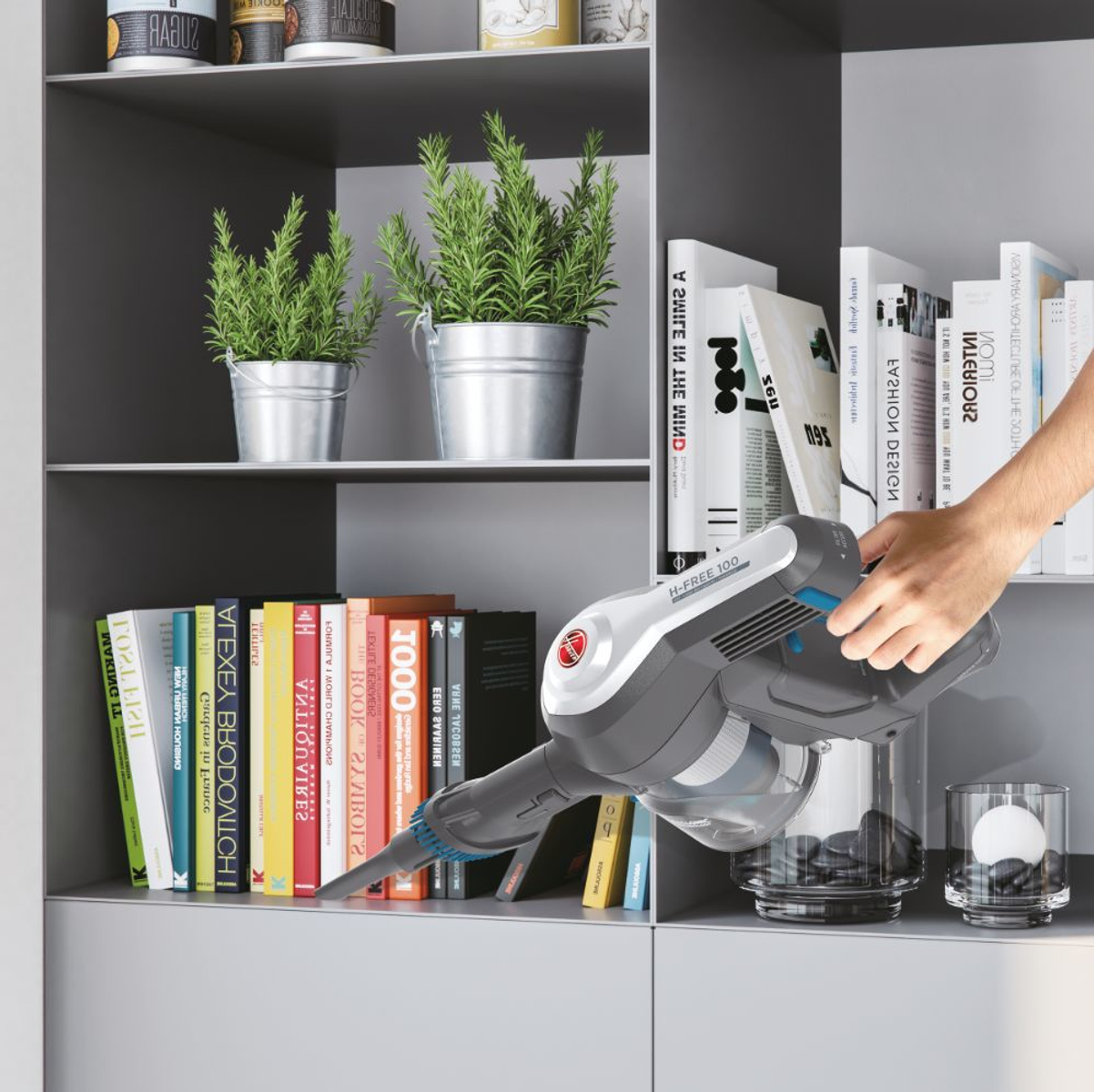 Handstaubsaugen eines Bücherregals mit Büchern, Topfpflanzen und Dekorationsartikeln.