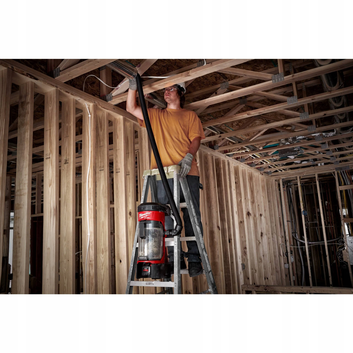 Uomo su una scala che usa un aspirapolvere per pulire un soffitto.