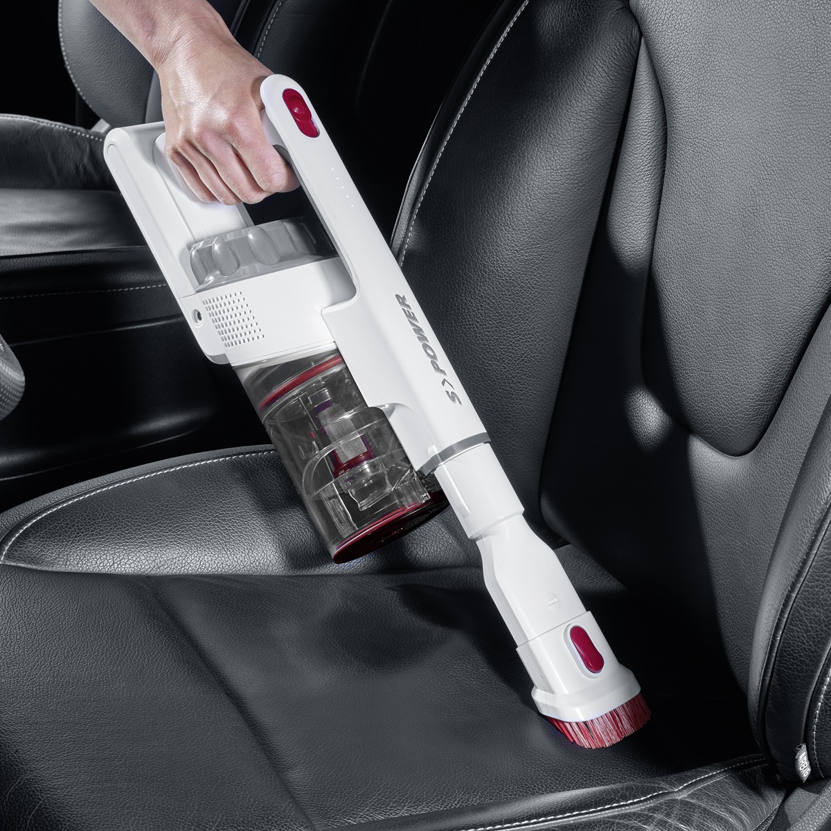 Aspirapolvere portatile bianco con testa rossa, che pulisce un sedile auto nero.
