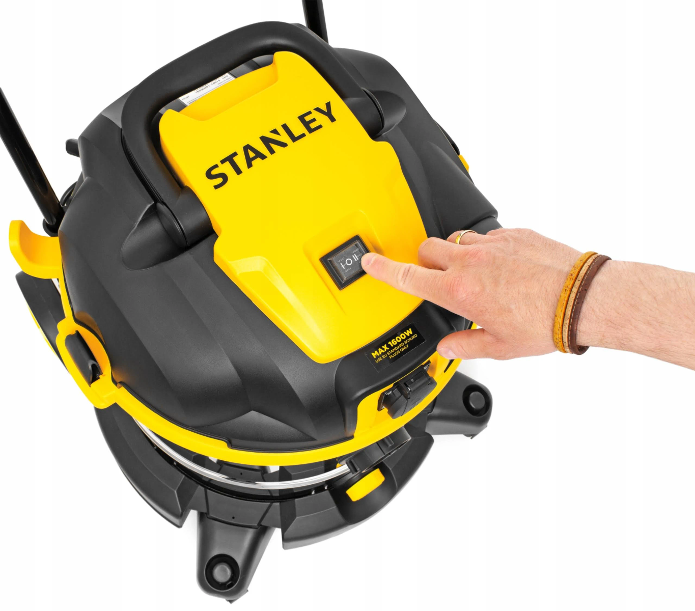 Vista superior de una aspiradora Stanley amarilla y negra. Una mano presiona el botón de encendido. Max 1800W.