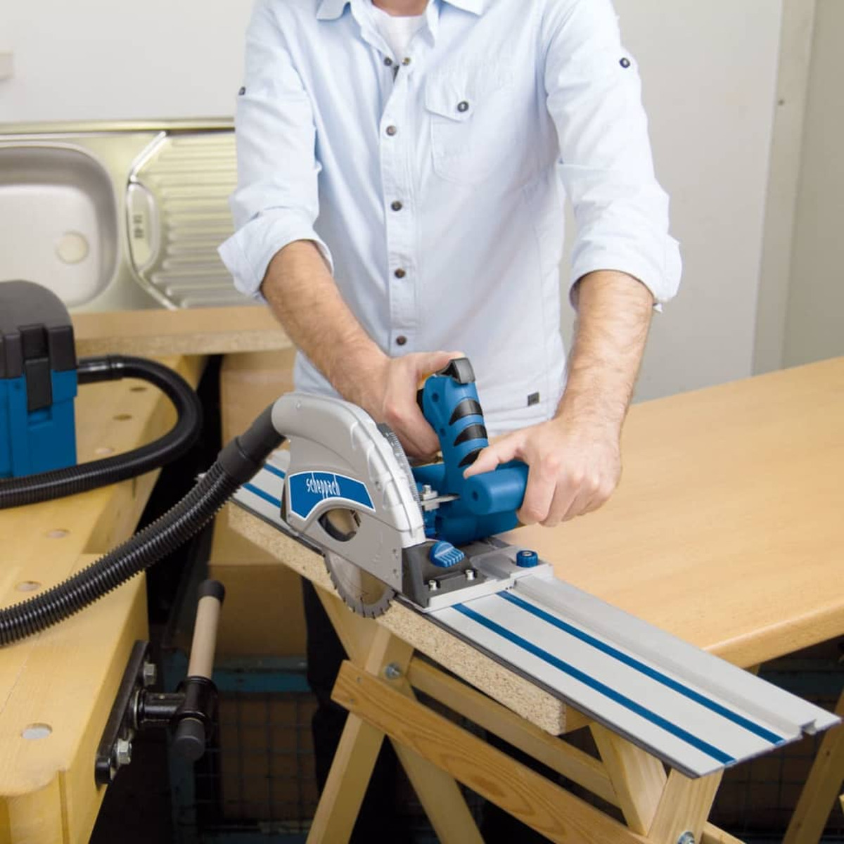 A man using a blue and silver circular saw on a wooden workbench.