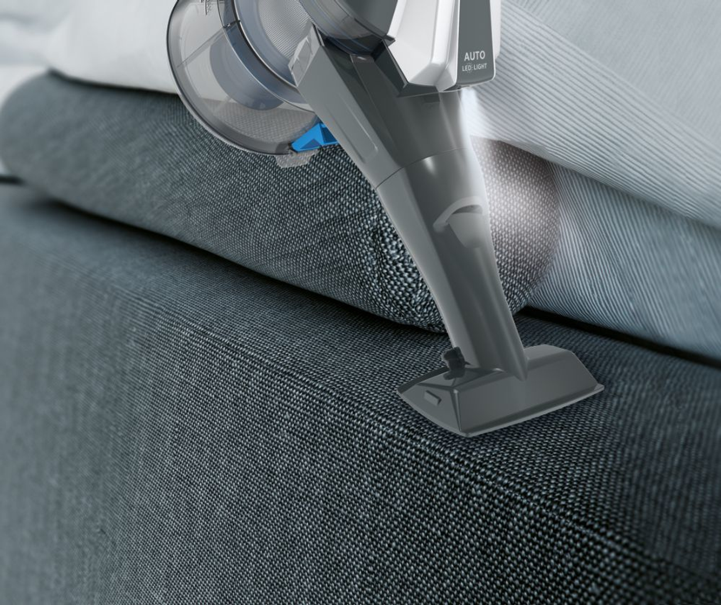 Un aspirapolvere portatile pulisce un divano grigio, con la luce LED accesa e un ugello nero.